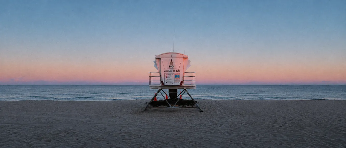 A Fort Lauderdale lifeguard stand at dusk, closed for the day, with the Atlantic calm and pink along the horizon behind it.